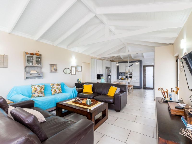 Spacious open-plan living area featuring a vaulted timber ceiling with exposed trusses, tiled flooring, and a modern kitchen with integrated appliances.