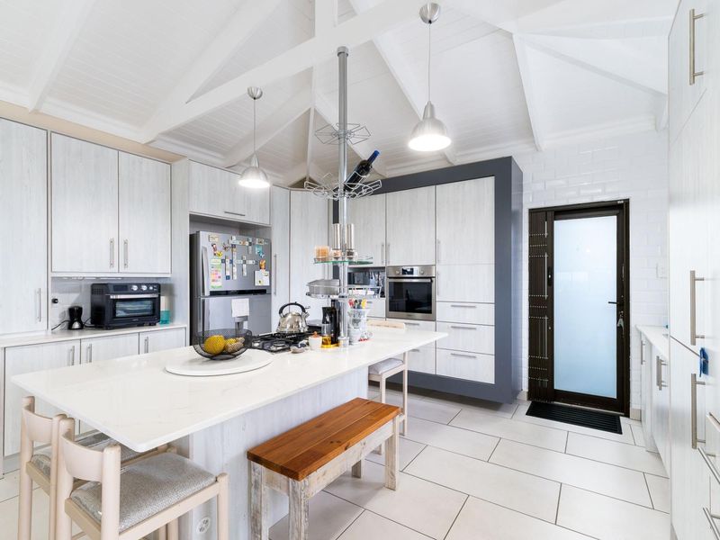 Modern kitchen featuring a central island with stone countertops, vaulted ceilings, built-in oven, gas hob, and tiled flooring with direct exterior access.