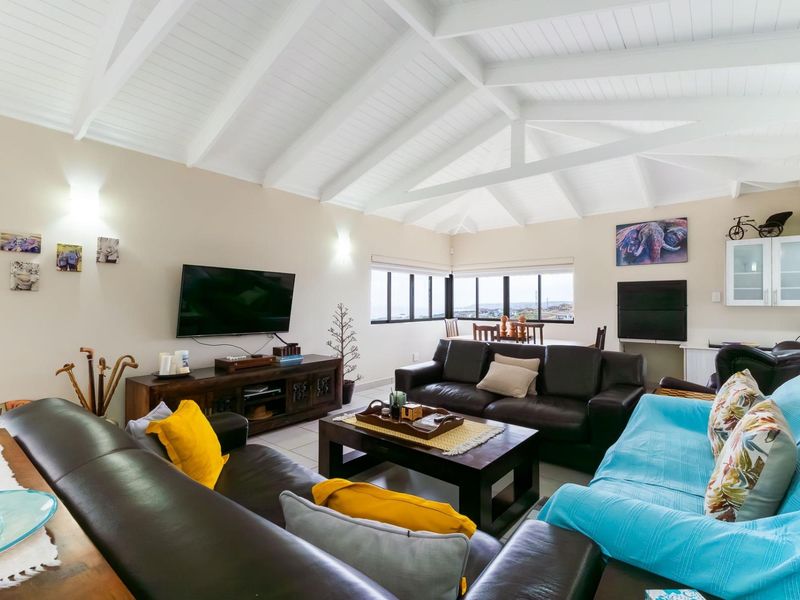 Spacious open-plan living area featuring a high vaulted ceiling with exposed white timber beams, tiled flooring, and large windows providing natural light.