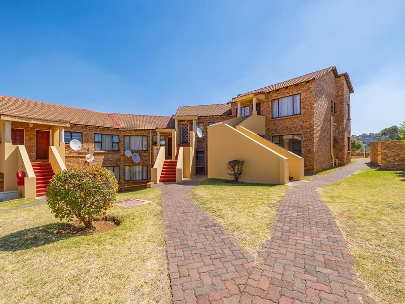 A well-maintained townhouse complex featuring face-brick exteriors, tiled roofs, and paved walkways leading to multiple residential entrances.