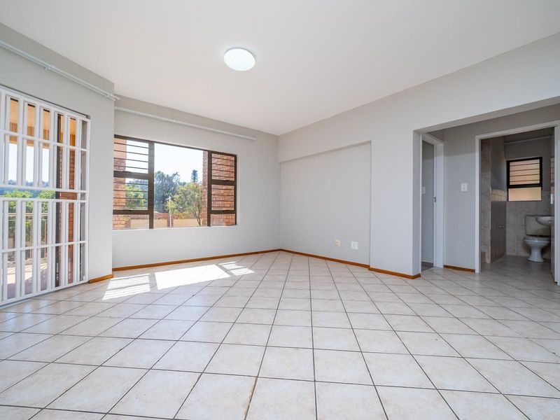 A bright, empty living area featuring neutral tiled flooring, large windows for natural light, and direct access to an outdoor space via a security gate.