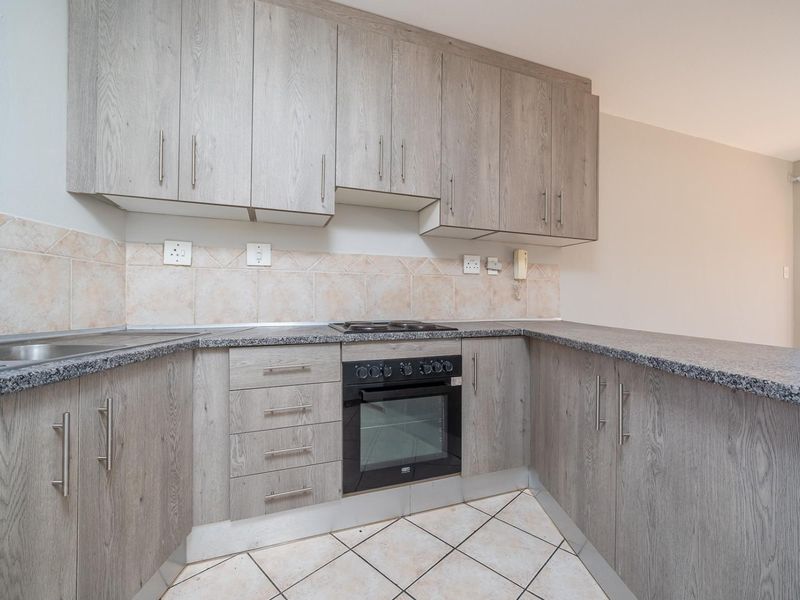 A functional kitchen featuring light wood-grain cabinetry, granite countertops, a built-in oven and hob, and tiled flooring.