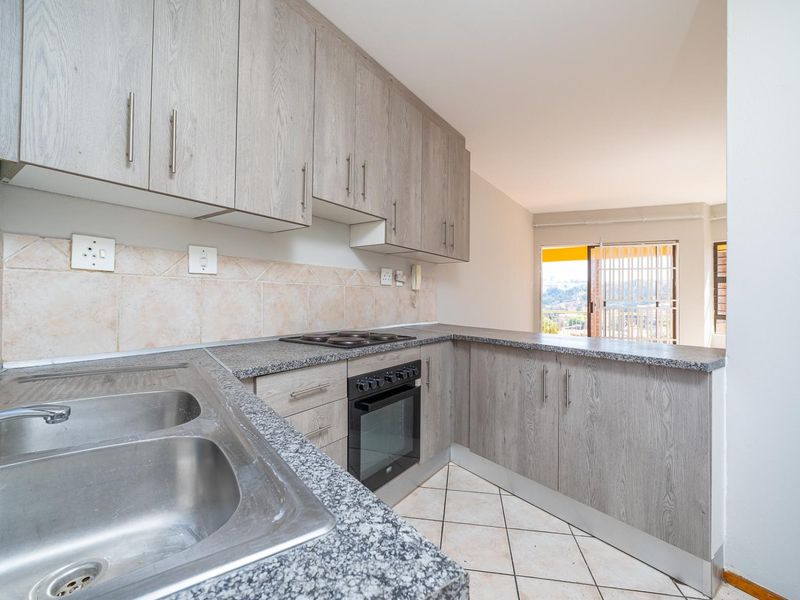 A functional kitchen featuring light wood-grain cabinetry, granite countertops, a double stainless steel sink, and built-in oven with electric hob.