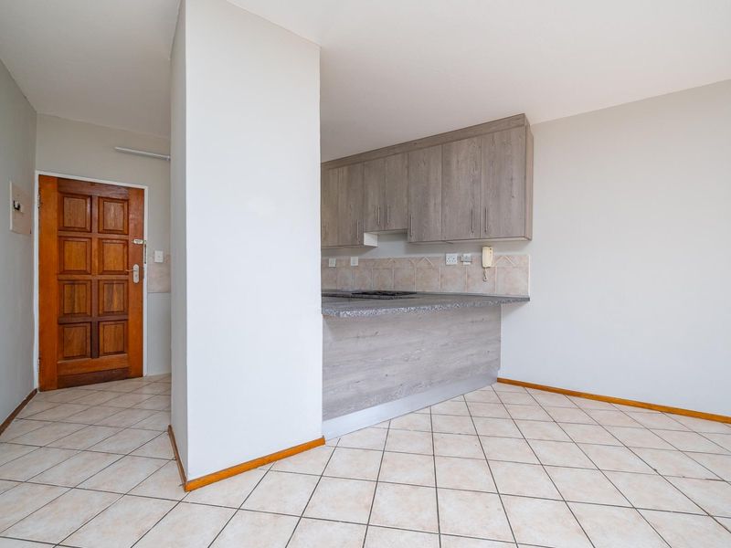 A functional kitchen area featuring built-in cabinetry, laminate countertops, and a tiled backsplash, adjacent to the main entrance with tiled flooring throughout.