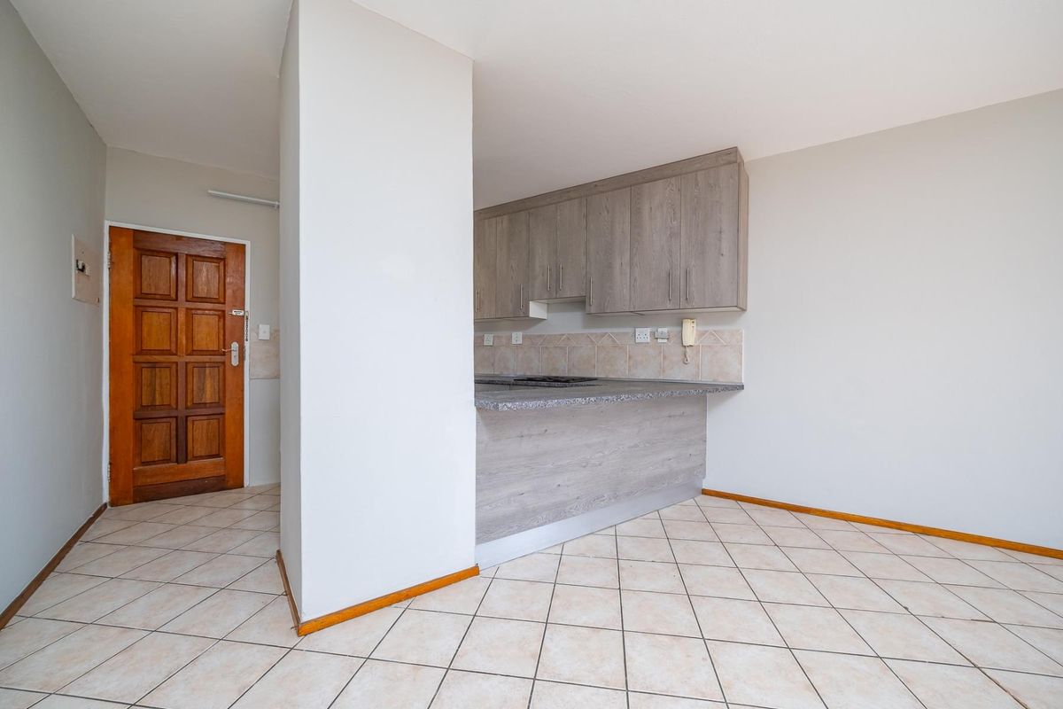 A functional kitchen area featuring built-in cabinetry, laminate countertops, and a tiled backsplash, adjacent to the main entrance with tiled flooring throughout.
