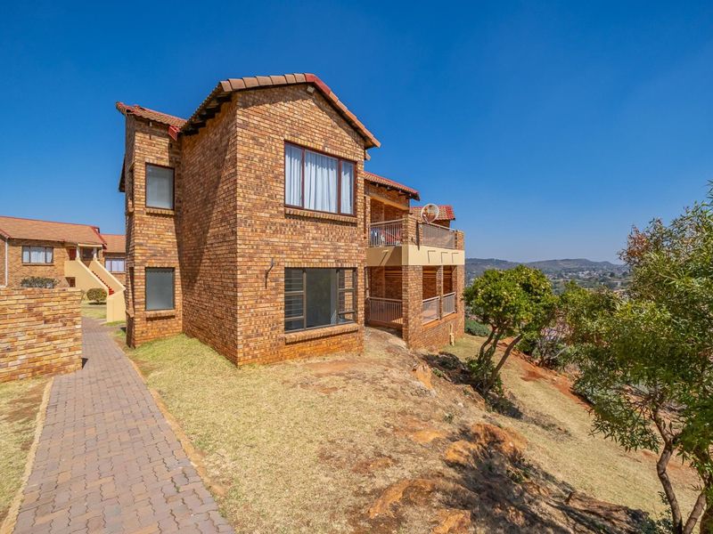Rear view of a face brick townhouse featuring a paved walkway, balcony with metal railings, and elevated views of the surrounding landscape.
