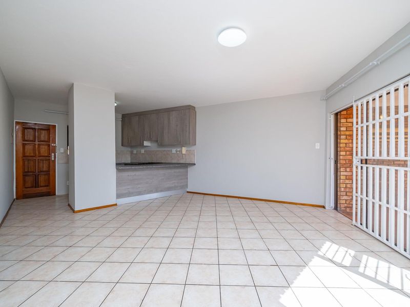 An open-plan living and kitchen area featuring ceramic tile flooring, built-in cabinetry with a breakfast counter, and direct access to an outdoor space.