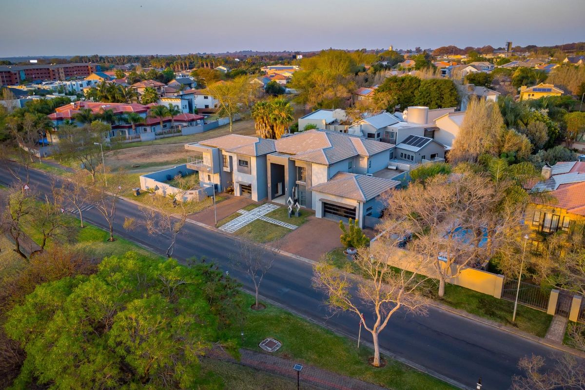 Aerial view of a modern residential property featuring a tiled roof, paved driveway, double garage, and solar panels within a suburban neighborhood setting.