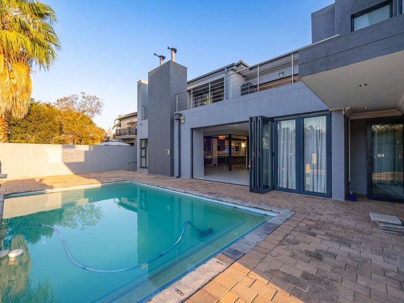 Modern rear exterior featuring a swimming pool, paved patio area, and large bi-fold doors opening into the main living space.