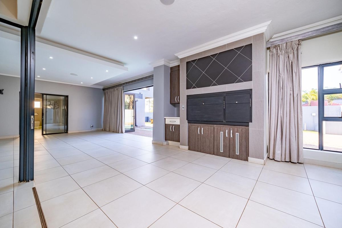 Spacious living area featuring large format floor tiles, recessed lighting, and a built-in braai with integrated cabinetry, opening onto an outdoor patio space.