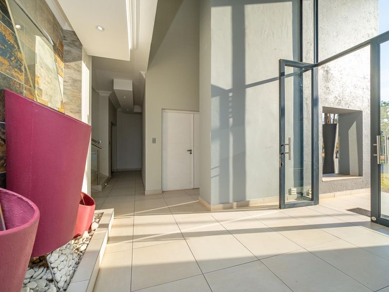 Modern entrance hall featuring large format floor tiles, a striking stone feature wall with a built-in water feature, and a grand glass pivot door.