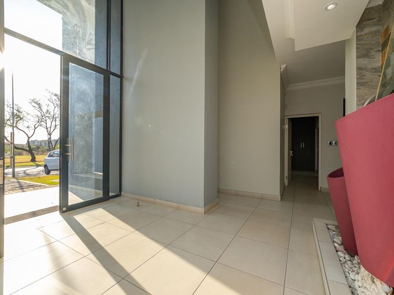 Spacious entrance hall featuring large glass pivot doors, tiled flooring, and a modern stone feature wall, providing a bright and welcoming transition area.
