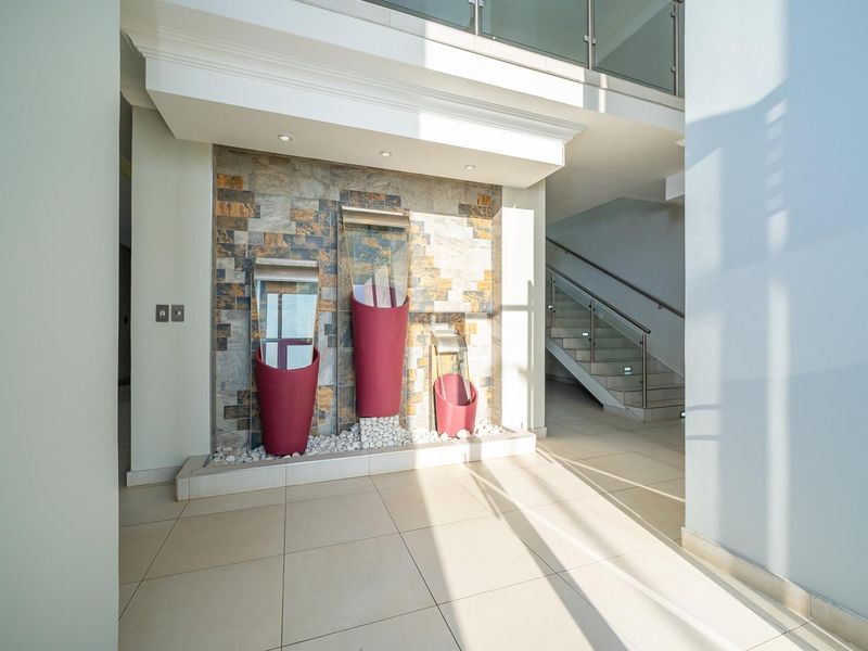 A bright and modern entrance hall featuring a decorative stone feature wall, tiled flooring, and a staircase with a contemporary glass balustrade.