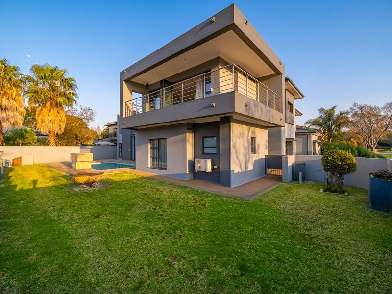 Rear view of a modern double-story house featuring a swimming pool, paved patio area, and an upper-level balcony with stainless steel railings.
