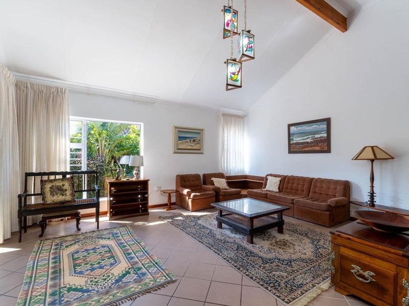Spacious living room featuring a high vaulted ceiling with exposed timber beam, tiled flooring, and large windows providing natural light and garden views.