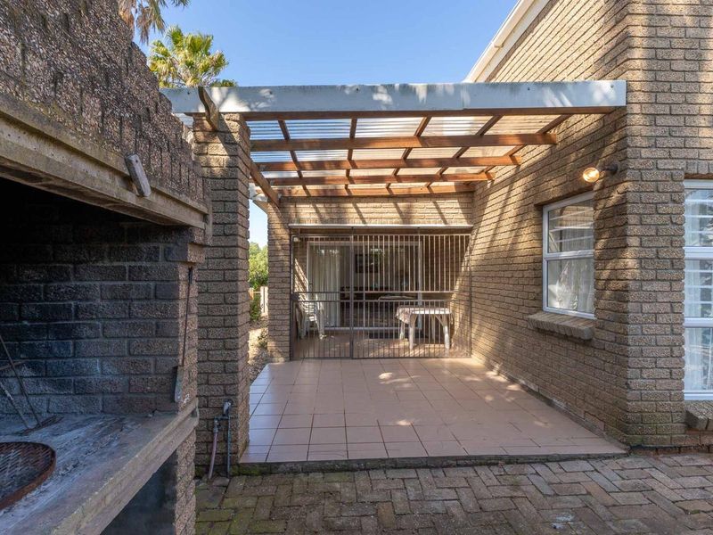 Outdoor patio area featuring a built-in brick braai, tiled flooring, and a timber pergola structure, providing a functional space for outdoor entertaining.