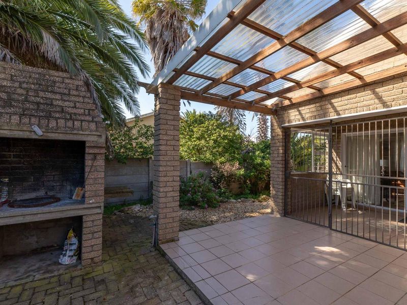 Covered outdoor patio area featuring a built-in brick braai, tiled flooring, and a pergola structure, providing a functional space for outdoor entertaining.