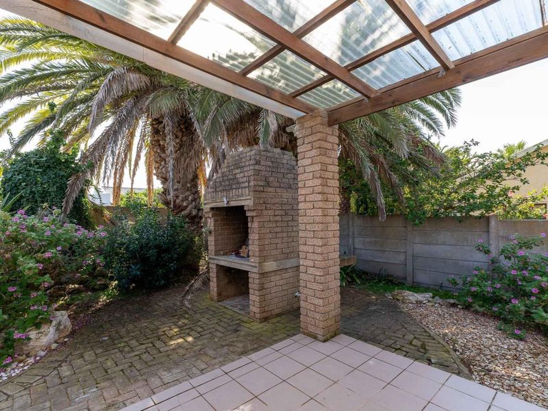 Outdoor patio area featuring a built-in brick braai, paved flooring, and a timber pergola with polycarbonate roofing, set within a private garden space.