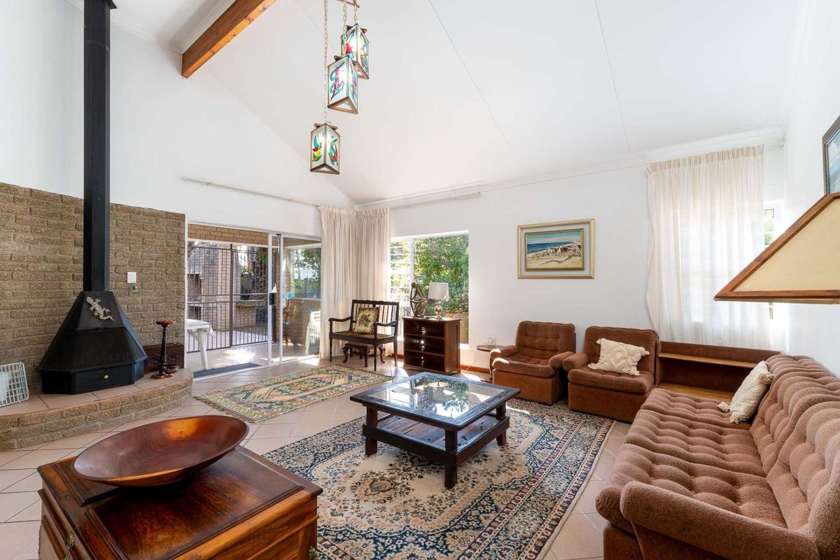 Spacious living room featuring a vaulted ceiling with exposed timber beams, a brick fireplace, and large sliding glass doors leading to the patio.