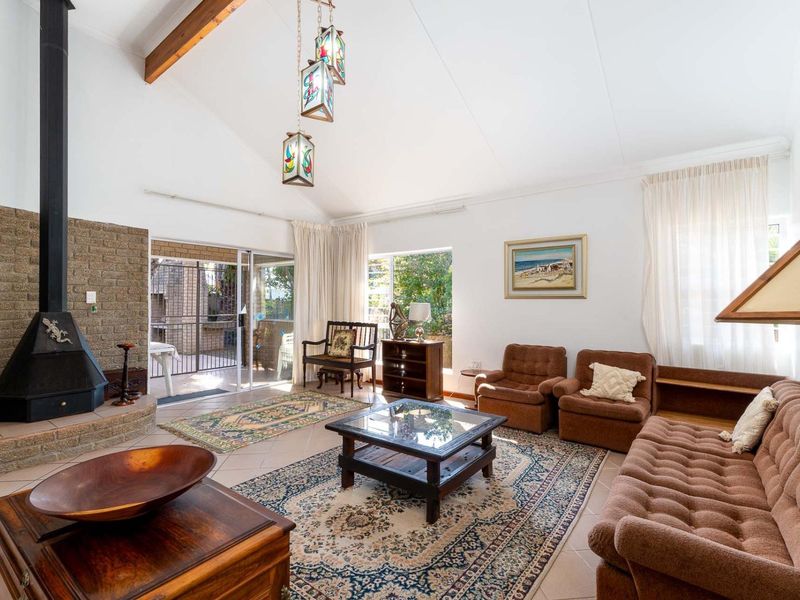 Spacious living room featuring a vaulted ceiling with exposed timber beams, a brick fireplace, and large sliding glass doors leading to the patio.