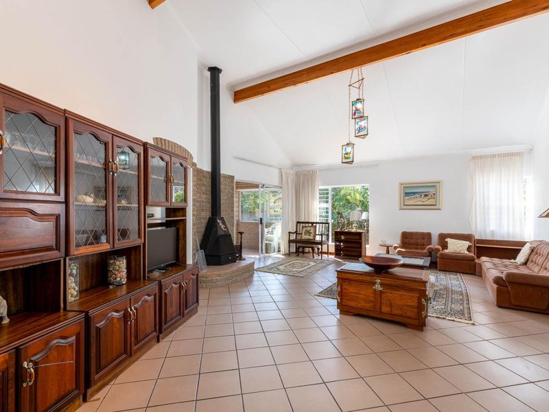 Spacious living room featuring vaulted ceilings with exposed timber beams, tiled flooring, and a prominent freestanding fireplace with a brick hearth.