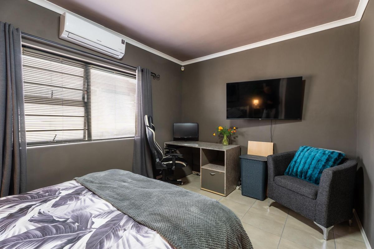 A well-maintained bedroom featuring tiled flooring, neutral wall tones, and a wall-mounted split-system air conditioning unit.