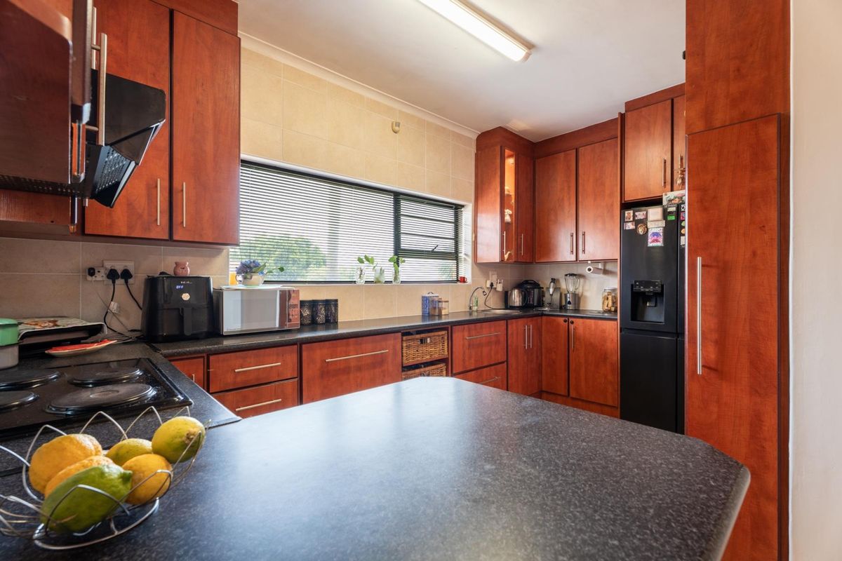 A functional kitchen featuring warm-toned wooden cabinetry, dark laminate countertops, a built-in electric hob, and a tiled backsplash.