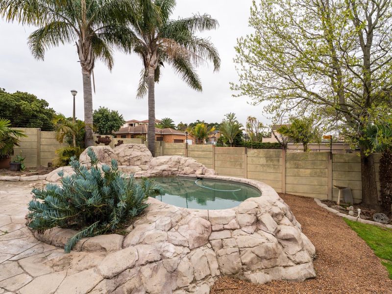 Outdoor pool area featuring a naturalistic rock-style swimming pool, paved surround, and established palm trees enclosed by a precast concrete boundary wall.