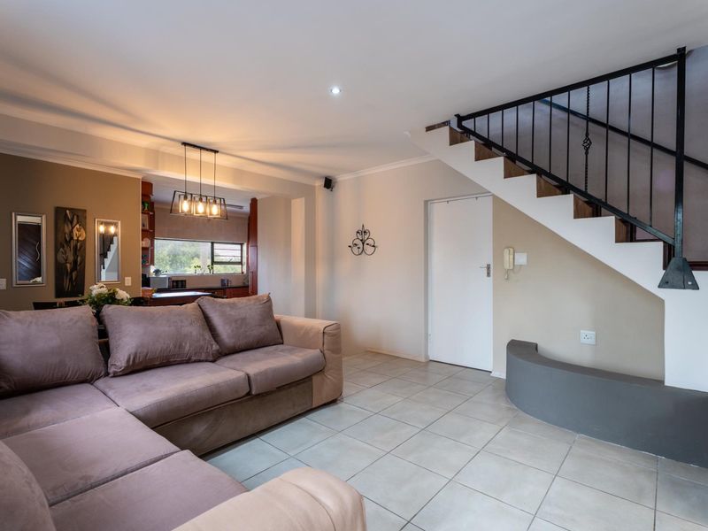 Open plan living area featuring tiled flooring, a staircase with a wrought iron balustrade, and a view through to the kitchen area.