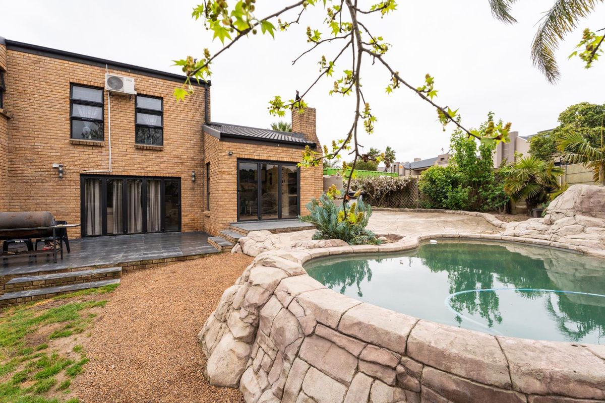 Rear exterior view featuring a brick facade, tiled patio area, and a rock-feature swimming pool set within a landscaped garden.