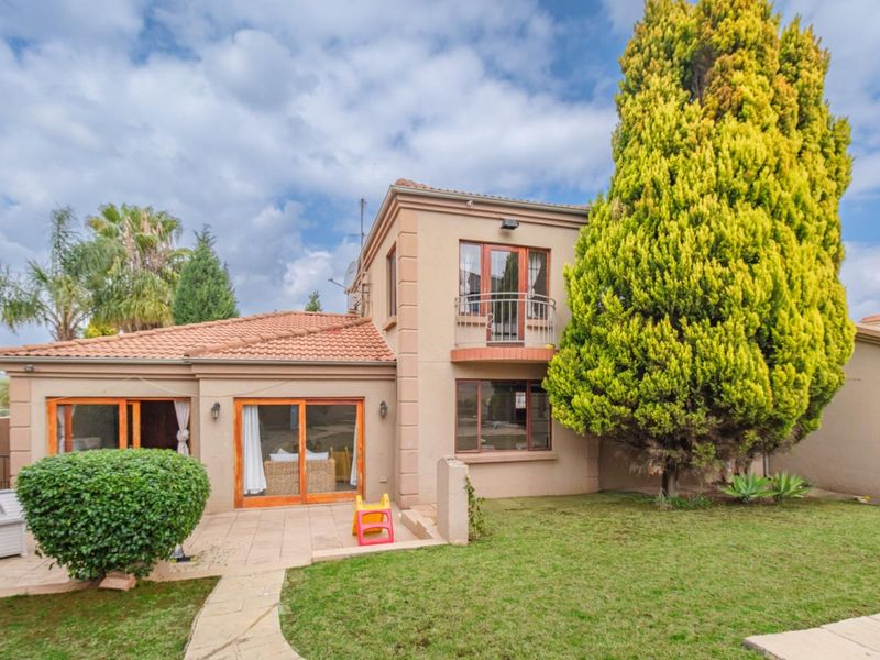 Rear view of a two-story townhouse featuring a paved patio, sliding glass doors, a small upper-level balcony, and a well-maintained garden area.