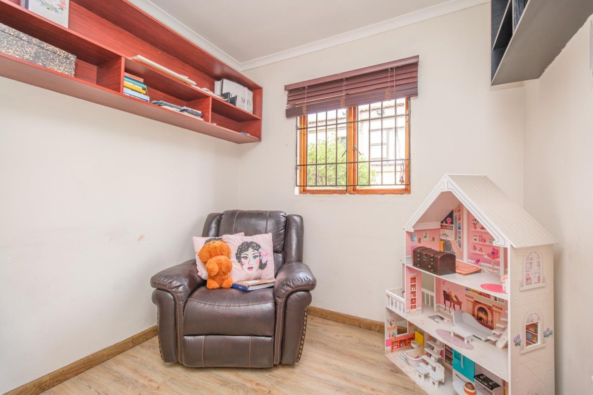 A bedroom featuring laminate flooring, built-in wall shelving, and a window fitted with security bars and venetian blinds.