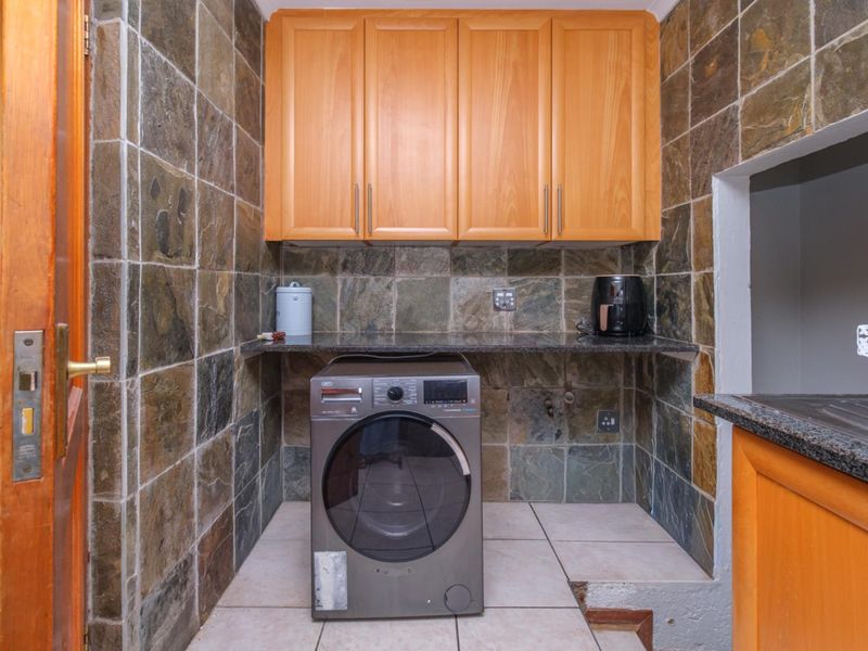 A functional laundry area featuring stone wall tiling, built-in wooden cabinetry, and a stone countertop with space for a washing machine.