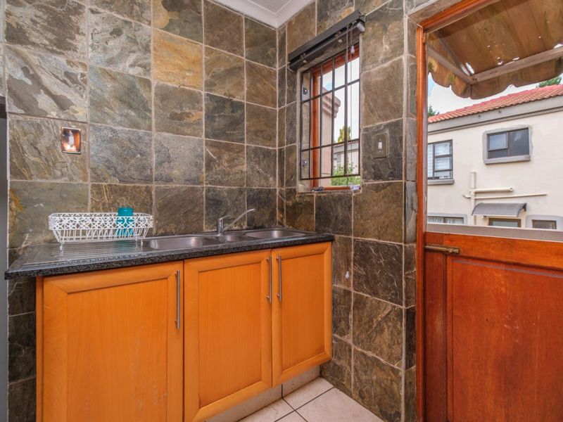 A functional scullery area featuring slate wall tiles, laminate cabinetry, and a double stainless steel sink with direct access to the exterior.