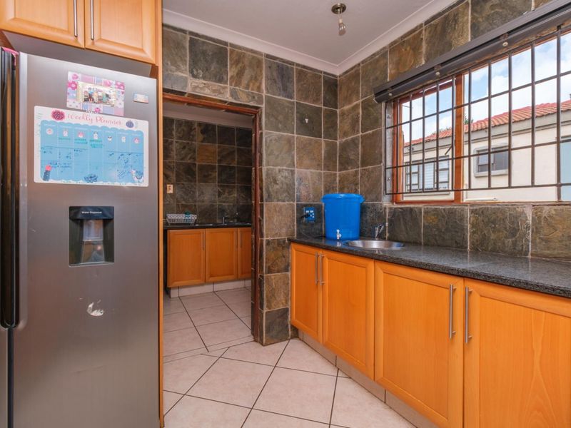 A functional scullery featuring wooden cabinetry, granite countertops, a stainless steel sink, and slate wall tiling, providing additional prep and wash-up space.