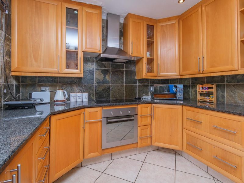 A functional kitchen featuring warm-toned wooden cabinetry, granite countertops, a built-in oven, and a stone tile backsplash.