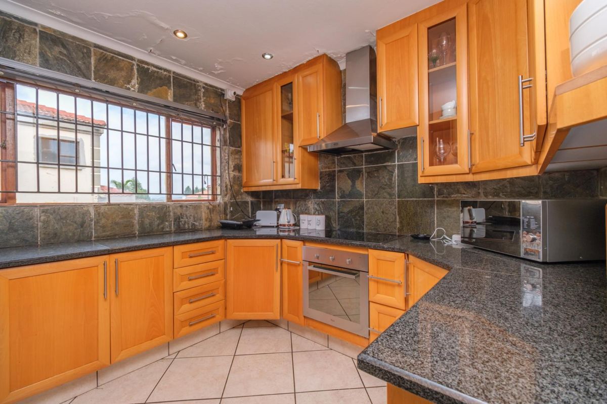 A functional kitchen featuring wooden cabinetry, granite countertops, built-in oven, and a stone tile backsplash. The ceiling requires maintenance and repair.