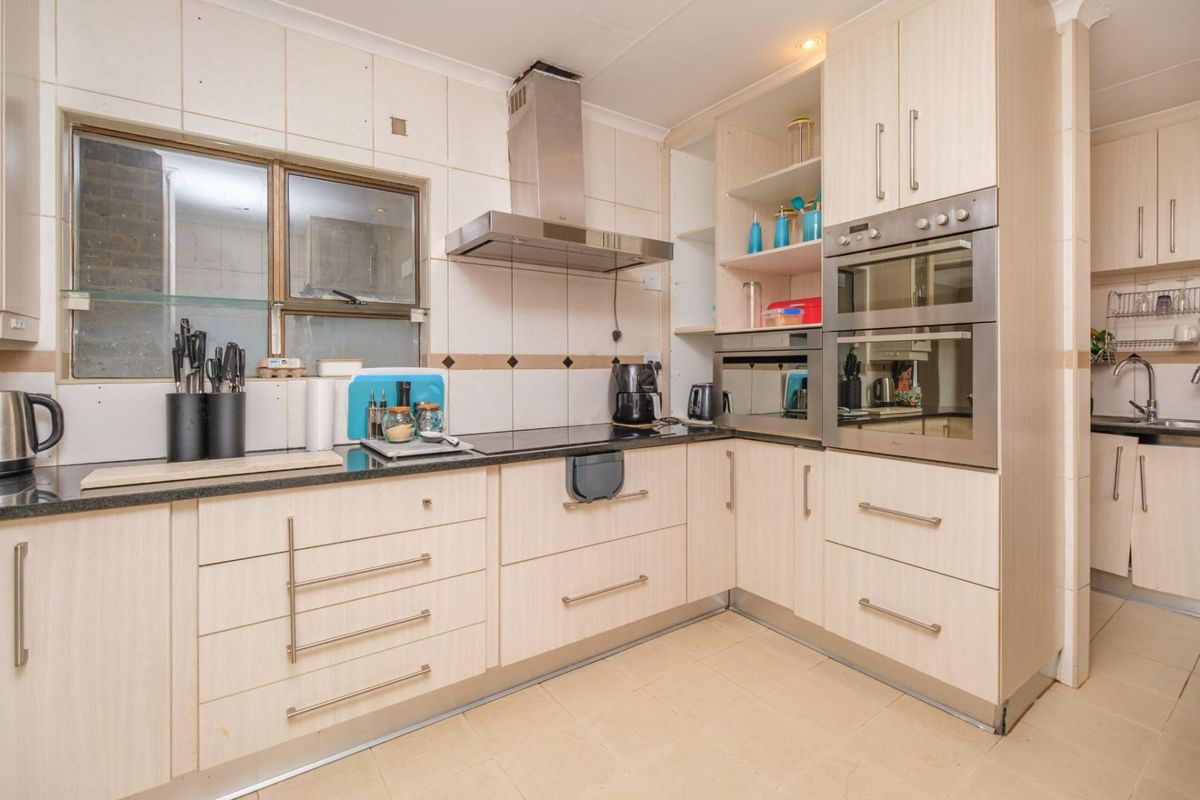 A functional kitchen featuring light wood cabinetry, built-in oven and microwave, stainless steel extractor fan, and tiled backsplash with a secondary scullery area.