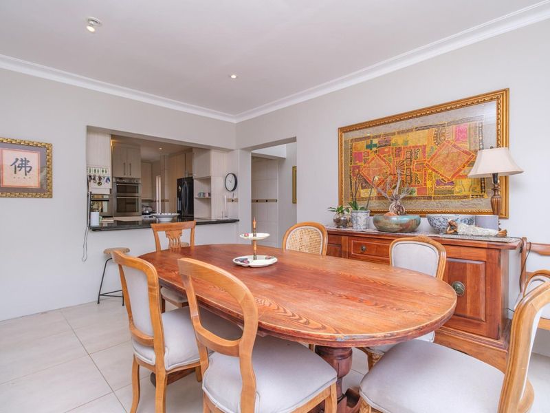 A bright dining room featuring tiled flooring, coved ceilings, and a convenient pass-through window connecting to the kitchen area.