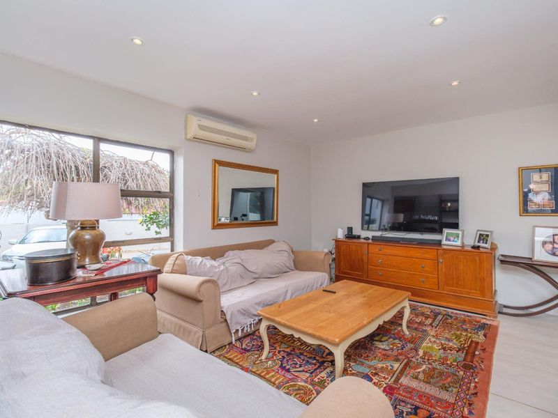 A comfortable living room featuring tiled flooring, recessed downlighting, and a wall-mounted split-system air conditioning unit, with large windows providing natural light.