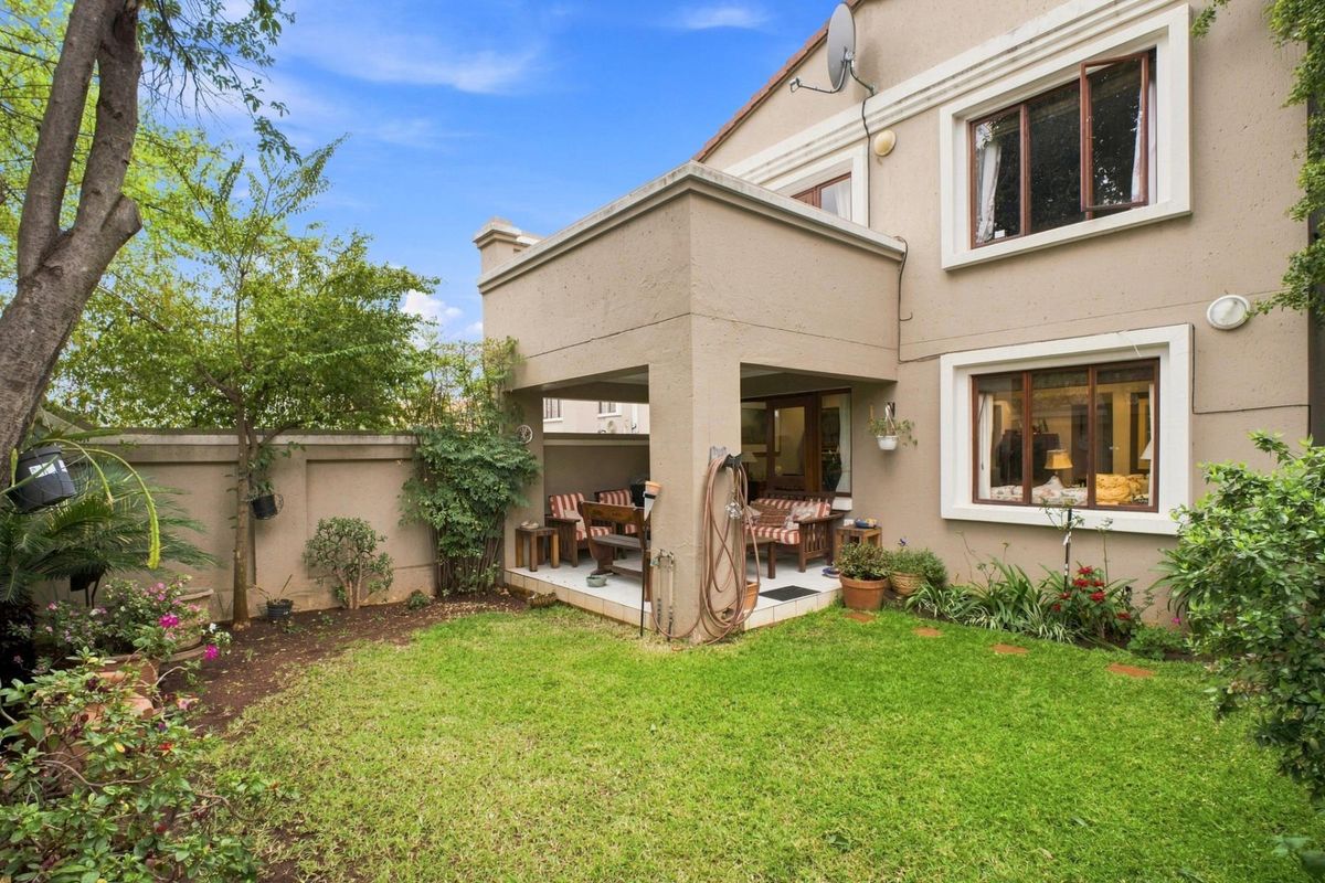 Rear view of the property featuring a covered patio area, a well-maintained lawn, and established garden borders with boundary walling.