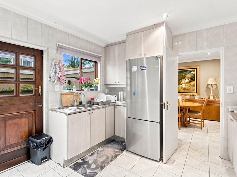 A functional kitchen featuring light-toned cabinetry, tiled surfaces, and direct access to the dining area.