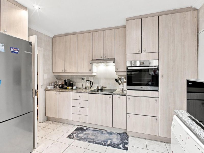 A functional kitchen featuring light wood-finish cabinetry, granite countertops, integrated oven, and electric hob with tiled flooring and backsplash.
