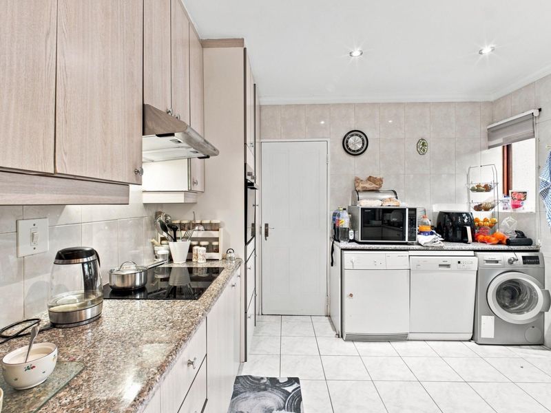 A functional kitchen featuring light wood-finish cabinetry, granite countertops, an electric hob with extractor, and tiled flooring with integrated laundry appliance space.