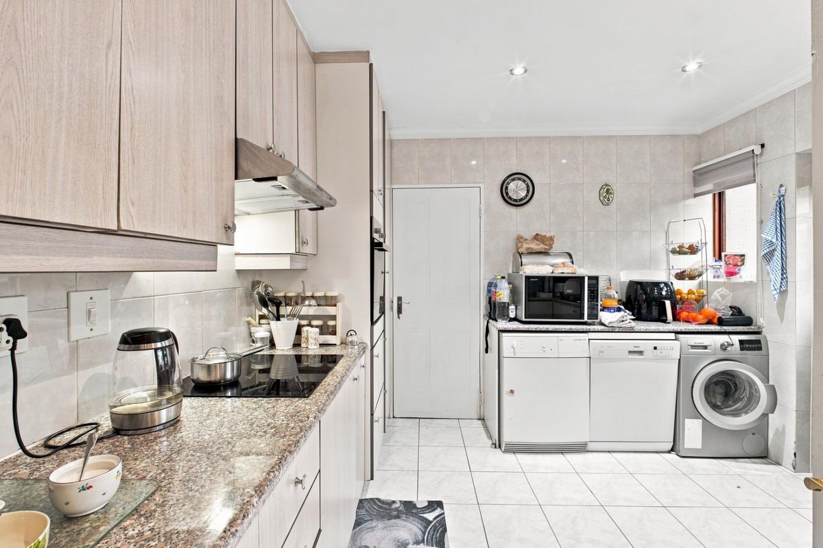 A functional kitchen featuring light wood-finish cabinetry, granite countertops, an electric hob with extractor, and tiled flooring with integrated laundry appliance space.