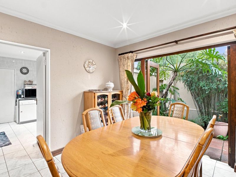 Dining room featuring tiled flooring and direct access to an outdoor patio area through wooden doors, with an adjacent view into the kitchen.