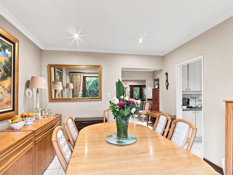 A well-lit dining room featuring tiled flooring, coving, and recessed downlights, with an open transition to the adjacent kitchen and living areas.
