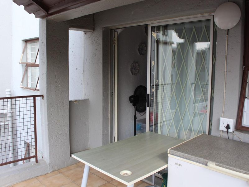 A covered balcony area featuring tiled flooring, a sliding glass door with security gate, and metal safety railings.