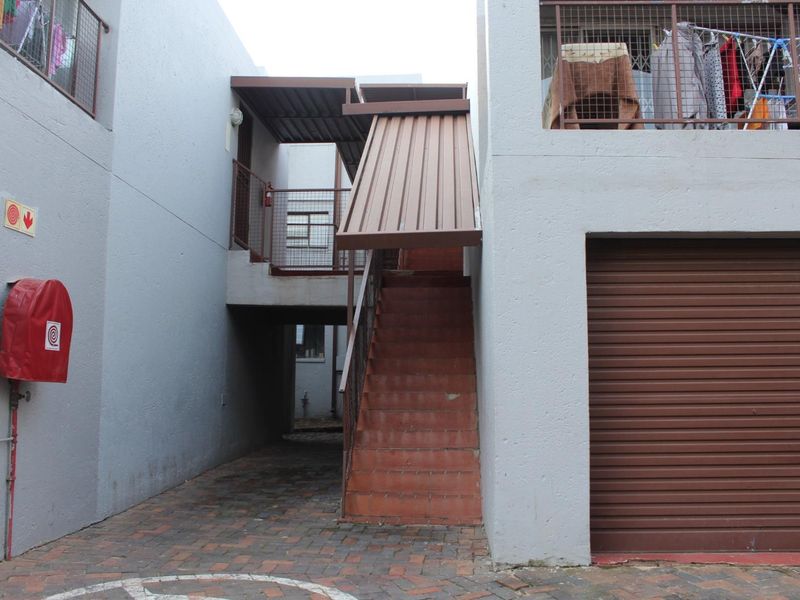 Exterior view of an apartment complex entrance featuring a paved driveway, metal staircase with awning, and a roller garage door.