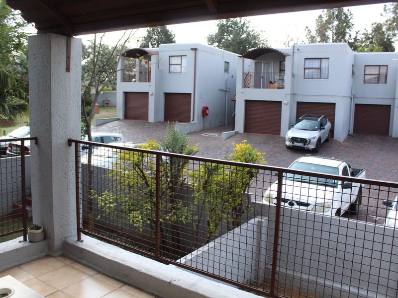 A covered balcony with tiled flooring and a metal mesh railing, overlooking the apartment complex parking area.